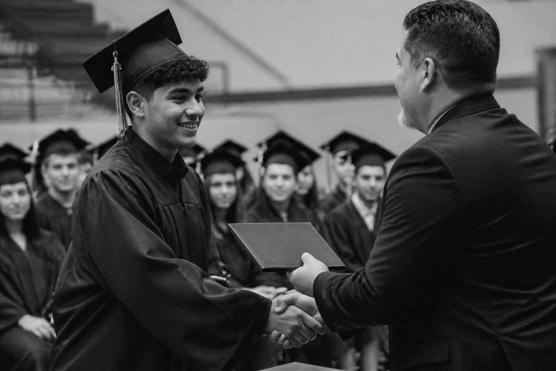 A high school senior shaking hands with an administrator while receiving a diploma cover at graduation